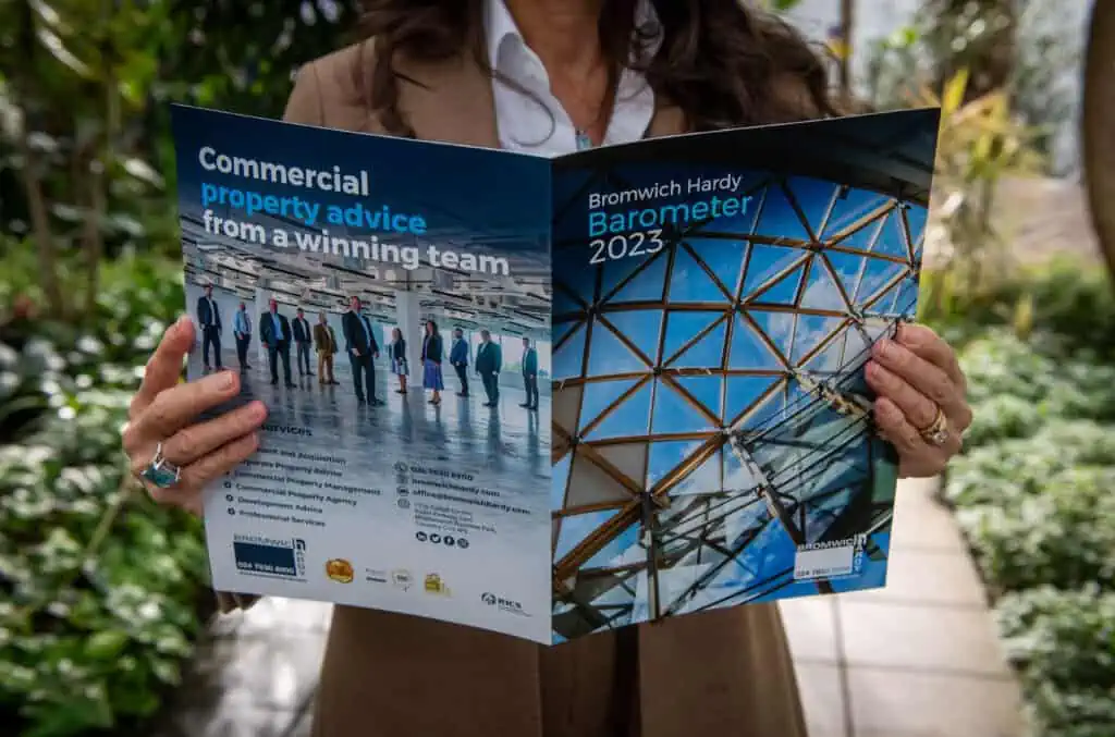 A female holding a copy of the 2023 Bromwich Hardy Barometer document in a leafy environment. Her face is not visible.